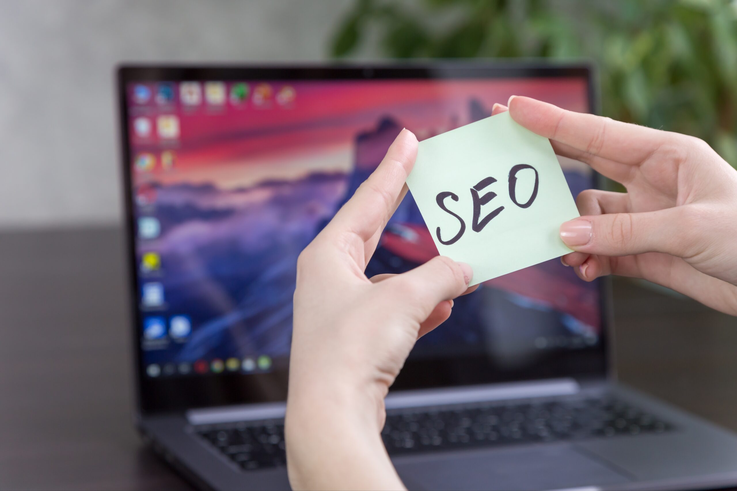 Manos sosteniendo nota con la palabra SEO frente a un portátil — estrategia de posicionamiento web